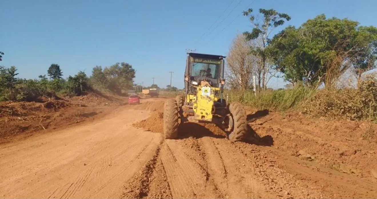 Motoniveladora com a lâmina no solo regularizando estrada de terra
