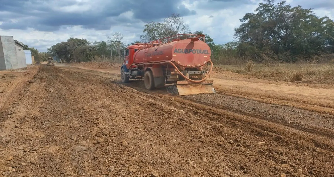 Caminhão-pipa umedecendo a base de estrada em obra, com motoniveladora ao fundo